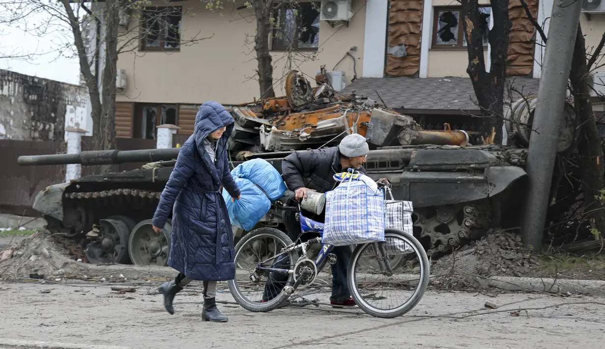 Warga sipil berjalan melewati tank yang hancur selama pertempuran sengit di daerah yang dikendalikan oleh pasukan separatis yang didukung Rusia di Mariupol, Ukraina, Selasa (19/4/2022).  engambil Mariupol akan membuat Ukraina kehilangan pelabuhan vital dan menyelesaikan. (AP Photo/Alexei Alexandrov)
