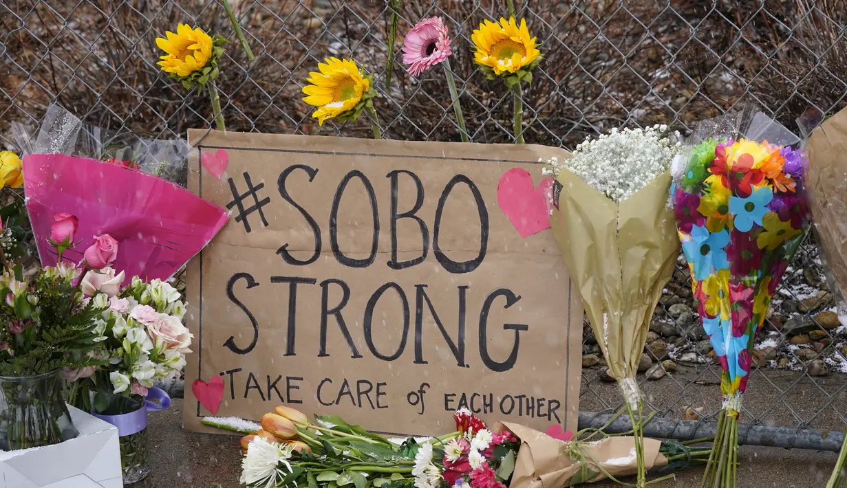 Tanda dari penduduk Boulder selatan berdiri di tengah karangan bunga yang ditinggalkan di sepanjang pagar yang dipasang di sekitar tempat parkir tempat penembakan massal terjadi di toko kelontong King Soopers di Boulder, Colorado (23/3/2021). (AP Photo/David Zalubowski)