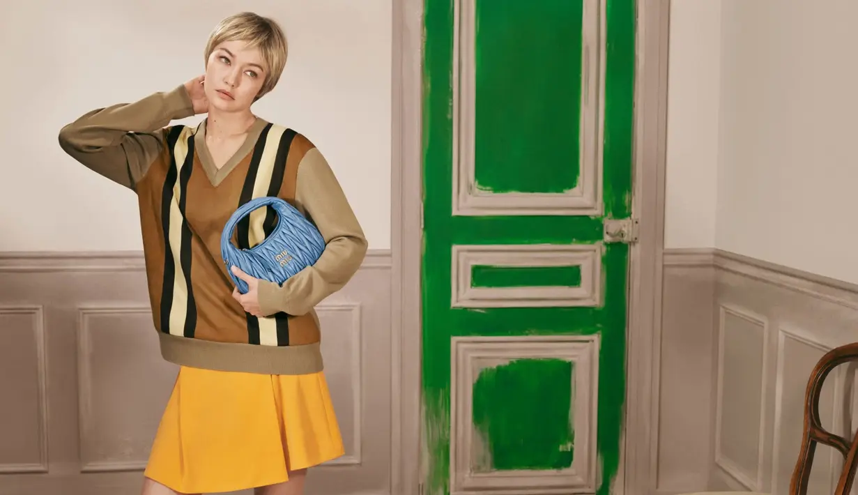 Pada foto lain, ibu Khai itu tampil lebih preppy lewat blazer suede cokelat, cropped blouse putih, serta rok navy berpotongan A-line. Tas hijau terang yang ia jinjing membuat keseluruhan look terasa lebih segar dan playful. [Dok/Miu Miu].