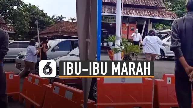 Seorang ibu-ibu mengenakan seragam putih membawa tongkat sambil marah-marah kepada seorang SPG.