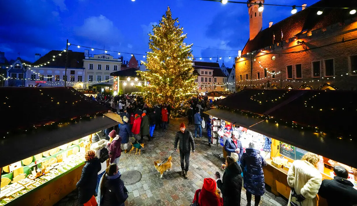 Seorang pria berjalan dengan seekor anjing di Pasar Natal di Alun-Alun Balai Kota, Tallinn, Estonia, 24 Desember 2022. (AP Photo/Pavel Golovkin)