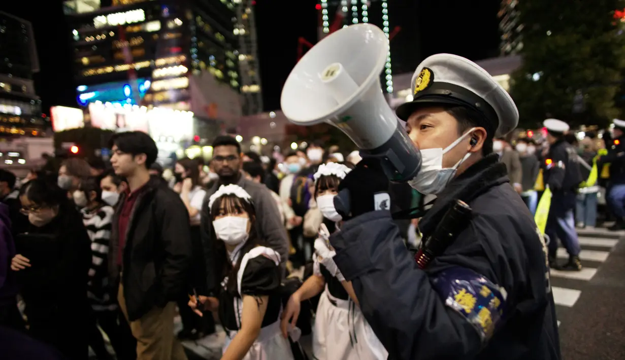 Polisi mendesak pejalan kaki dengan kostum untuk terus bergerak menyeberangi persimpangan jalan yang terkenal saat perayaan Halloween di distrik hiburan Shibuya, Tokyo, Jepang, 31 Oktober 2022. Polisi dikerahkan untuk patroli mengendalikan kerumunan saat perayaan Halloween di Shibuya. (AP Photo/Hiro Komae)