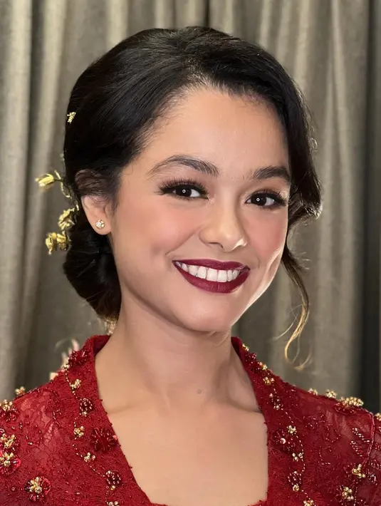 Mutiara terlihat anggun dalam balutan kebaya merah marun berekor panjang. Kesan elegan terpancar dari penggunaan mote-mote emas pada kebaya kutu baru tersebut. (Instagram/ochiipramita)