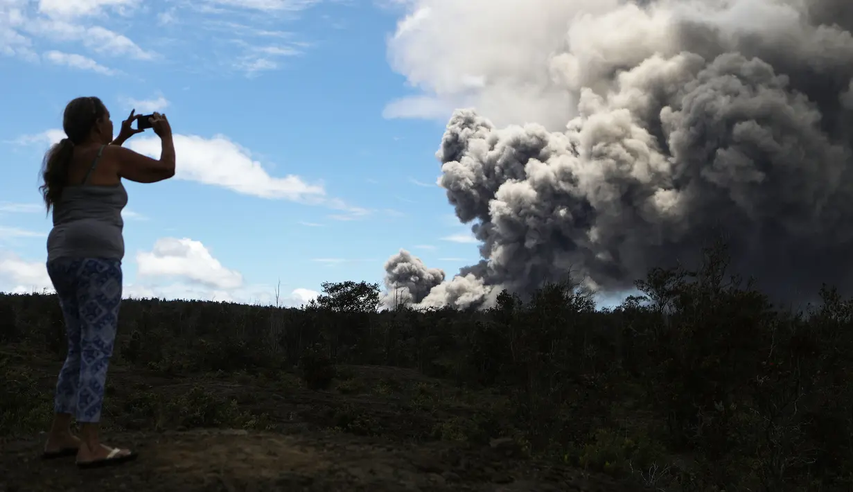 Seorang wanita mengambil gambar kepulan abu vulkanik dari gunung berapi Kilauea di Big Island Hawaii (15/5). Sejauh ini, sudah ada 40 rumah dan bangunan lainnya yang hancur terkena lava yang dimuntahkan oleh gunung Kilauea. (Mario Tama/Getty Images/AFP)