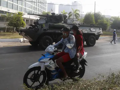 Pengendara sepeda motor melintas melewati kendaraan lapis baja yang dikerahkan di luar gedung Bank Sentral Myanmar di Yangon, Senin (15/2/2021). Pasukan militer Myanmar mulai menerjunkan kendaraan lapis baja di kota-kota besar di Myanmar dan memutus akses internet. (AP Photo)