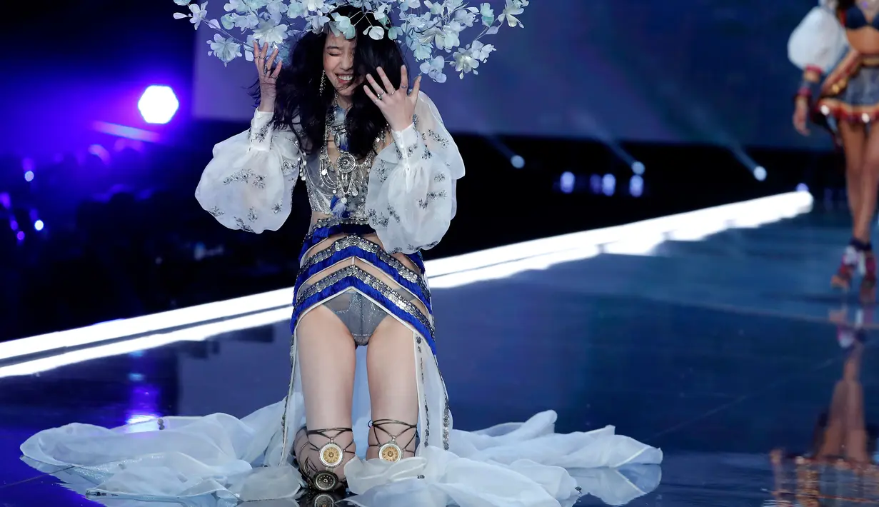 Model Tiongkok, Ming Xi terduduk di atas catwalk setelah jatuh tergelincir pada Victoria’s Secret Fashion Show 2017 di Shanghai, Senin (20/11). Ming yang mengenakan stiletto boots kemungkinan menginjak jubahnya sendiri yang panjang. (AP/Andy Wong)