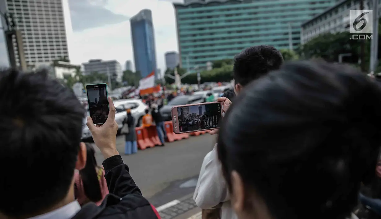 Warga menggunakan ponsel untuk mengambil gambar konvoi kemenangan Persija Jakarta merayakan keberhasilan menjadi juara Piala Presiden 2018 di kawasan Bundaran HI, Minggu (18/2). Lautan oranye memenuhi jalan-jalan di ibu kota. (Liputan6.com/Faizal Fanani)
