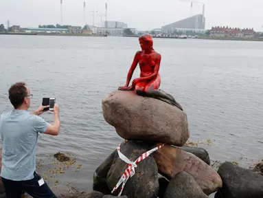 Turis memotret patung putri duyung 'Little Mermaid' yang menjadi korban vandalisme sekelompok aktivis lingkungan di Kopenhagen, Denmark, Selasa (30/5). Patung bersejarah dan jadi ikon itu memerah seolah bersimbah darah. (Jens Dresling/Ritzau Foto via AP)