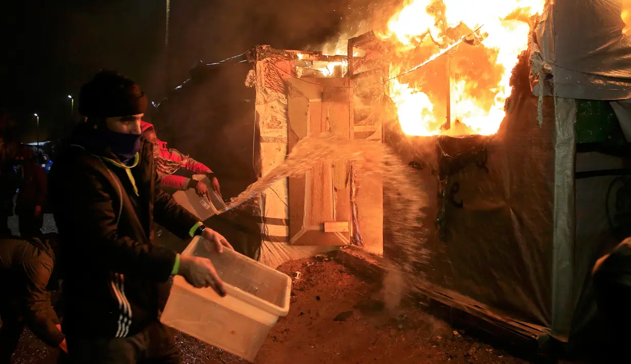 Imigran berusaha memadamkan api yang membakar kamp mereka di lahan kumuh yang dijuluki "Jungle" di Calais, Prancis (1/3). Kamp ini berpenghuni sekitar 3.000 pengungsi dan pencari suaka. (REUTERS/Pascal Rossignol)