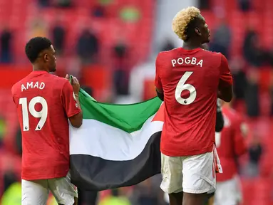 Gelandang Manchester United (MU), Amad Diallo (kiri) dan Paul Pogba mengibarkan bendera Palestina usai ditahan imbang Fulham pada pekan ke-37 Liga Inggris di Stadion Old Trafford, Rabu (19/5/2021) dinihari WIB. Pogba tampak diberikan bendera Palestina oleh seorang pendukung MU. (Paul ELLIS/POOL/AFP)