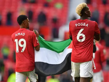 Gelandang Manchester United (MU), Amad Diallo (kiri) dan Paul Pogba mengibarkan bendera Palestina usai ditahan imbang Fulham pada pekan ke-37 Liga Inggris di Stadion Old Trafford, Rabu (19/5/2021) dinihari WIB. Pogba tampak diberikan bendera Palestina oleh seorang pendukung MU. (Paul ELLIS/POOL/AFP)