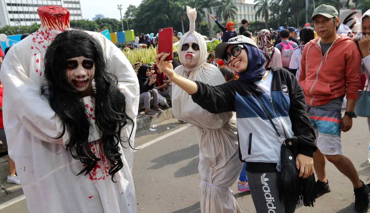 Warga berswafoto dengan seniman berkostum pocong saat kegiatan Car Free Day di Bundaran HI di Jakarta, Minggu, (12/11). Untuk dapat berswafoto warga dikenakan tarif semampunya. (Liputan6.com/Fery Pradolo)