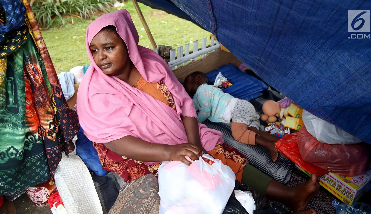 Seorang wanita pencari suaka termenung di samping anaknya yang tertidur di trotoar depan Rumah Detensi Imigrasi Kalideres, Jakarta, Jumat (19/1). Para pencari suaka berasal dari Afghanistan, Sudan, dan Somalia. (Liputan6.com/JohanTallo)