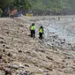 Polisi berdiri di antara sampah kiriman yang terdampar memenuhi pesisir pantai Kuta, Bali, Kamis (31/12/2020). Menjelang pergantian tahun baru, Pantai Kuta hanya terlihat beberapa wisatawan, namun tumpukan sampah kiriman tersebar di sepanjang bibir pantai. (SONNY TUMBELAKA / AFP)