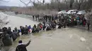Ribuan migran menyeberangi sungai dengan berpegangan pada seutas tali di perbatasan Yunani-Makedonia, Idomeni, Yunani (14/3/2016). Lebih dari 1.000 migran nekat menembus sungai untuk mencari jalan keluar perbatasan. (Reuters/Stoyan Nenov)