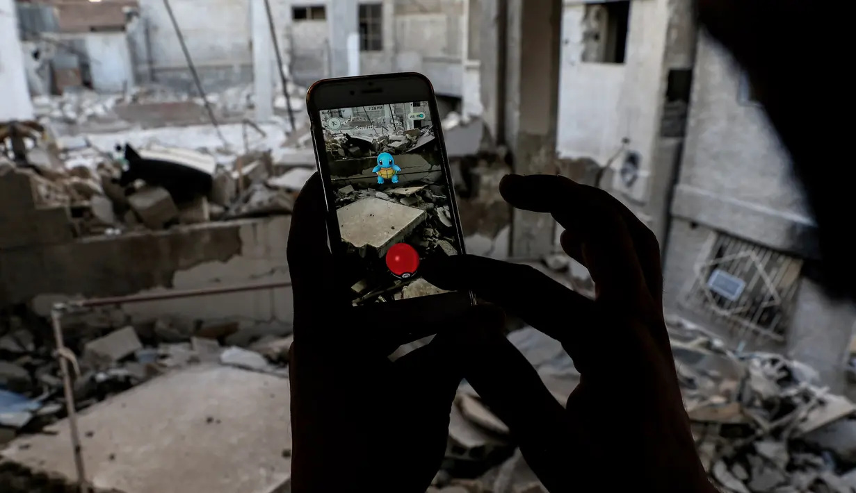 Seorang gamer Suriah menggunakan aplikasi Pokemon Go di ponselnya untuk mencari Pokemons di antara puing-puing di kota Douma, Damaskus (23/7). (AFP PHOTO / Sameer Al-Doumy)