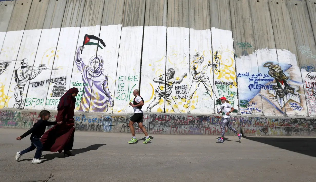 Peserta berlari menyusuri tembok pemisah Israel selama Right to Movement Maraton di kota Bethlehem, Palestina, Jumat (1/4). Tembok ini menjadi sarana bagi seniman jalanan untuk menuangkan keahliannya. (REUTERS / Ammar Awad)