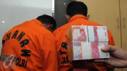 Dua tersangka beserta uang palsu pecahan Rp100 ribu diperlihatkan di Gedung Bareskrim, Jakarta, Senin (23/5). Pada prakteknya kedua tersangka ini mengedarkan uang palsu itu dengan modus menukarkan uang palsu dengan uang asli. (Liputan6.com/Helmi Afandi)