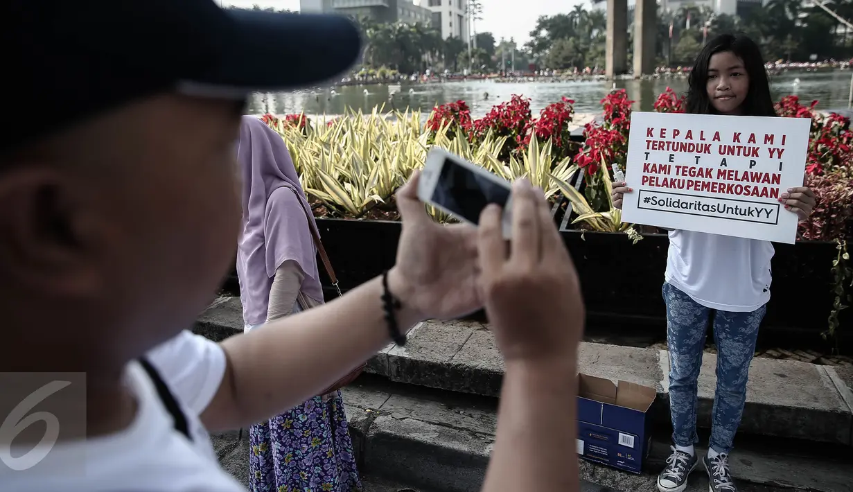 Seorang warga mengambil gambar peserta aksi solidaritas untuk Yuyun disela kegiatan car free day di Bundaran HI, Jakarta, Minggu (8/5). Aksi solidaritas untuk Yuyun itu pun berlangsung serentak di 13 kota lainnya. (Liputan6.com/Faizal Fanani)