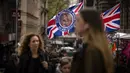 Pejalan kaki berjalan melewati kios yang menjual bendera yang mengumumkan penobatan Raja Charles di London, Jumat, 5 Mei 2023. Penobatan Raja Charles III akan berlangsung di Westminster Abbey pada 6 Mei. (AP Photo/Emilio Morenatti)