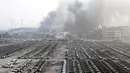 Kepulan asap masih terlihat diantara puing kendaraan di lokasi ledakan di pelabuhan Kota Tianjin, China, Kamis (13/8/2015). Ledakan yang diperkirakan berkekuatan setara 21 ton TNT ini menewaskan 17 orang dan ratusan lainya terluka. (REUTERS/China Daily)
