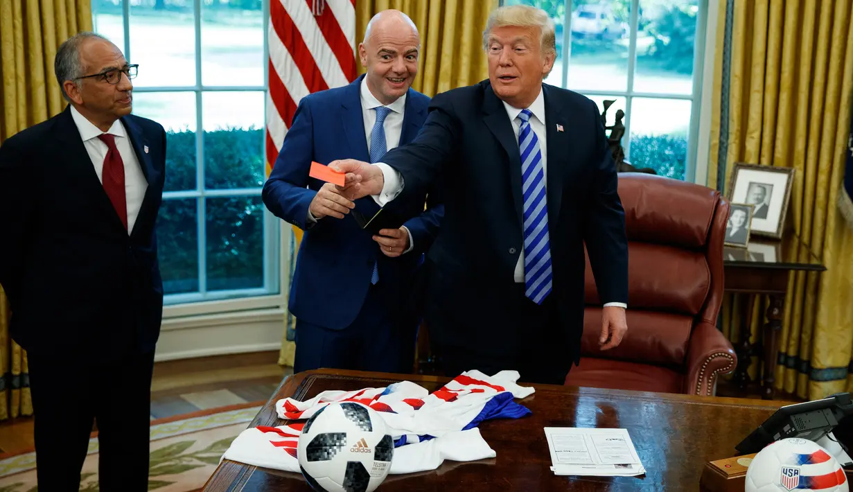 Presiden AS, Donald Trump menyodorkan kartu merah yang diberikan presiden FIFA, Gianni Infantino ke arah jurnalis yang meliput pertemuan mereka di Oval Office Gedung Putih pada Selasa (28/8). (AP/Evan Vucci)