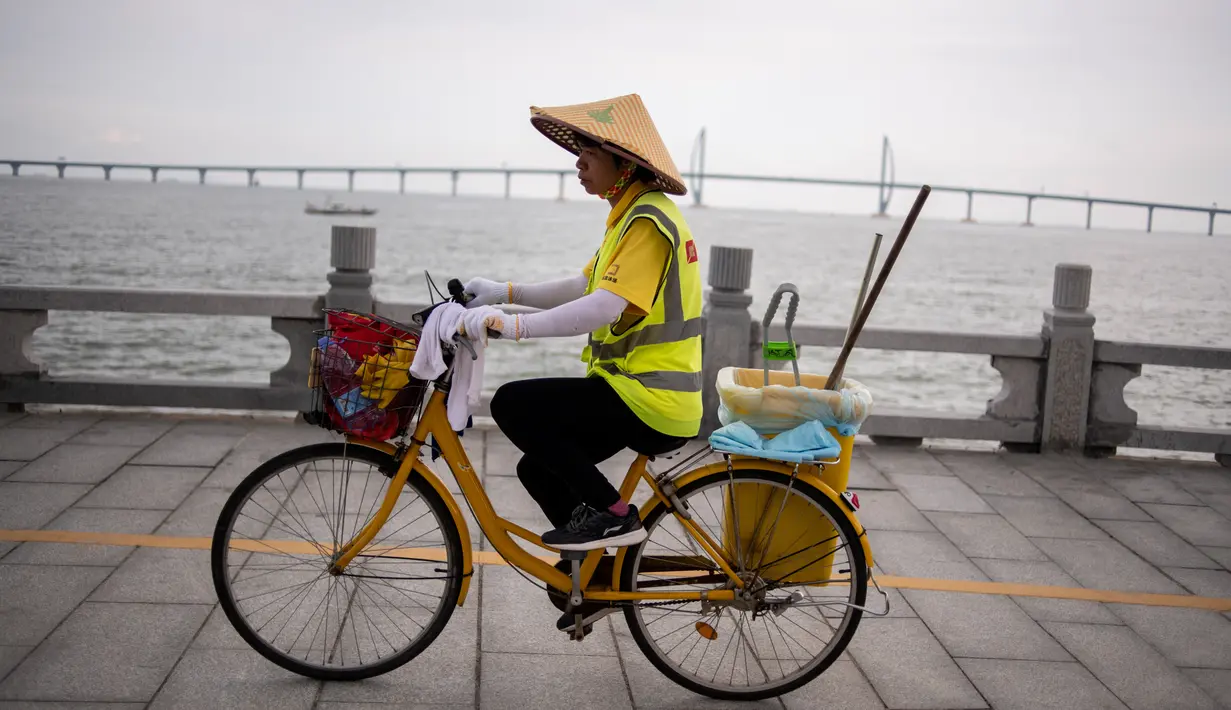 Petugas kebersihan mengendarai sepeda dengan latar Jembatan Hong Kong-Zhuhai-Makau (HKZM) di Zhuhai (22/10). Jembatan laut terpanjang di dunia yang menghubungkan Hong Kong, Makau, dan daratan Cina ini akan dibuka 24 Oktober 2018. (AFP Photo/Fred Dufour)