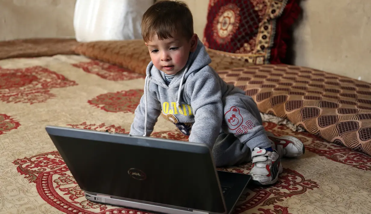 Bayi laki-laki berusia 18 bulan yang bernama Donald Trump bermain dengan laptop di rumah kontrakannya di Kabul, Kamis (15/3). Dengan menamai anaknya dengan nama Trump, Assadullah berharap putranya bisa meraih kesuksesan dalam hidup. (AP/Rahmat Gul)