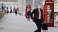 Seorang pria mengenakan masker untuk mengurangi penyebaran Covid-19, berjalan di sepanjang Whitehall di pusat kota London (5/1/2022). Rumah sakit Inggris telah kekurangan staf yang disebabkan oleh gelombang infeksi Omicron, kata pemerintah pada hari Selasa (4/1). (AFP/Tolga Akmen)