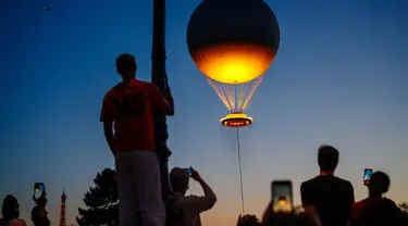 Orang-orang menyaksikan kaldron Olimpiade Paris 2024 saat matahari terbenam di Jardin des Tuileries di Paris pada 28 Juli 2024. (Dimitar DILKOFF/AFP)