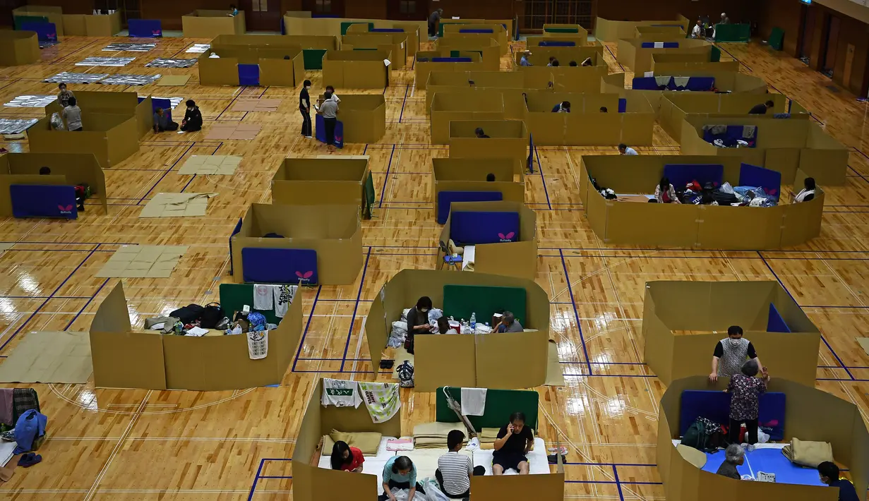 Penduduk setempat berlindung di pusat evakuasi dengan kotak kardus untuk menjaga jarak di sebuah gimnasium kota Yatsushiro di prefektur Kumamoto, Jepang, Senin (6/7/2020). Hujan deras menghambat operasi pencarian dan penyelamatan korban banjir dan tanah longsor di Kumamoto. (Charly TRIBALLEAU/AFP)