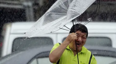 Seorang pria Taiwan memperbaiki payungnya saat melawan angin kencang yang ditimbulkan oleh topan Lekima di Taipei, Taiwan (9/8/2019). Topan Lekima saat ini tengah menghantam Taiwan, membawa angin ribut dengan kecepatan 190 km/jam. (AP Photo / Chiang Ying-ying)