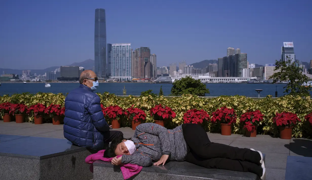 Sepasang suami istri beristirahat sambil mengenakan masker pelindung untuk mencegah penyebaran virus corona di tepi pantai melawan Victoria Habour di Hong Kong, Sabtu (2/1/2021). Hong Kong mengalami lonjakan jumlah kasus pada akhir November. (AP Photo/Vincent Yu)