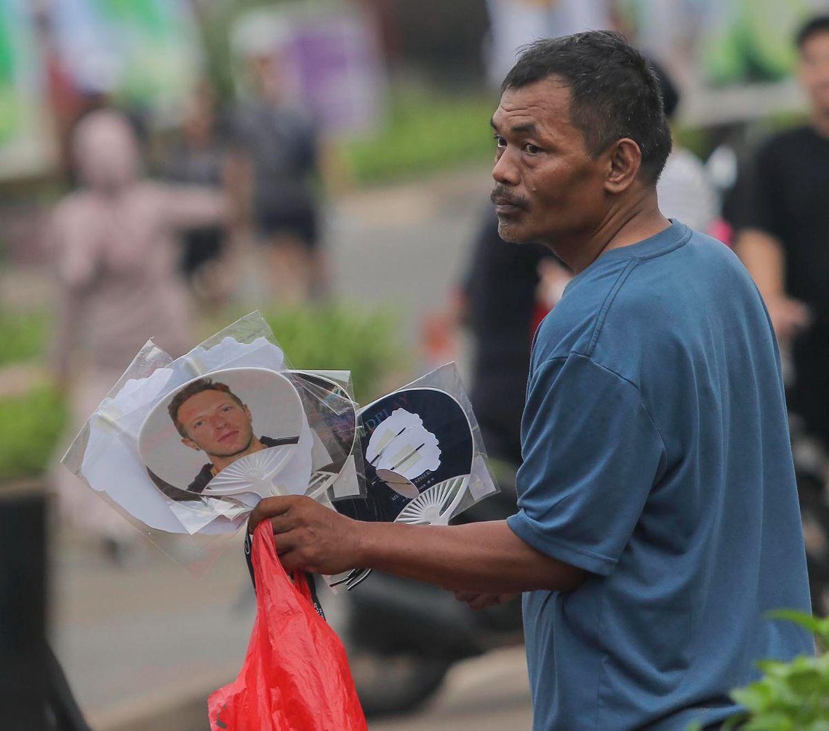 Seorang pedagang musiman menawarkan kipas bergambar Chris Martin, vokalis Coldplay, di sekitaran Gelora Bung Karno (GBK), Senayan, Jakarta, Rabu (15/11/2023). Konser Coldplay bertajuk 'Music of the Spheres Tour' yang berlangsung di Jakarta malam ini diman