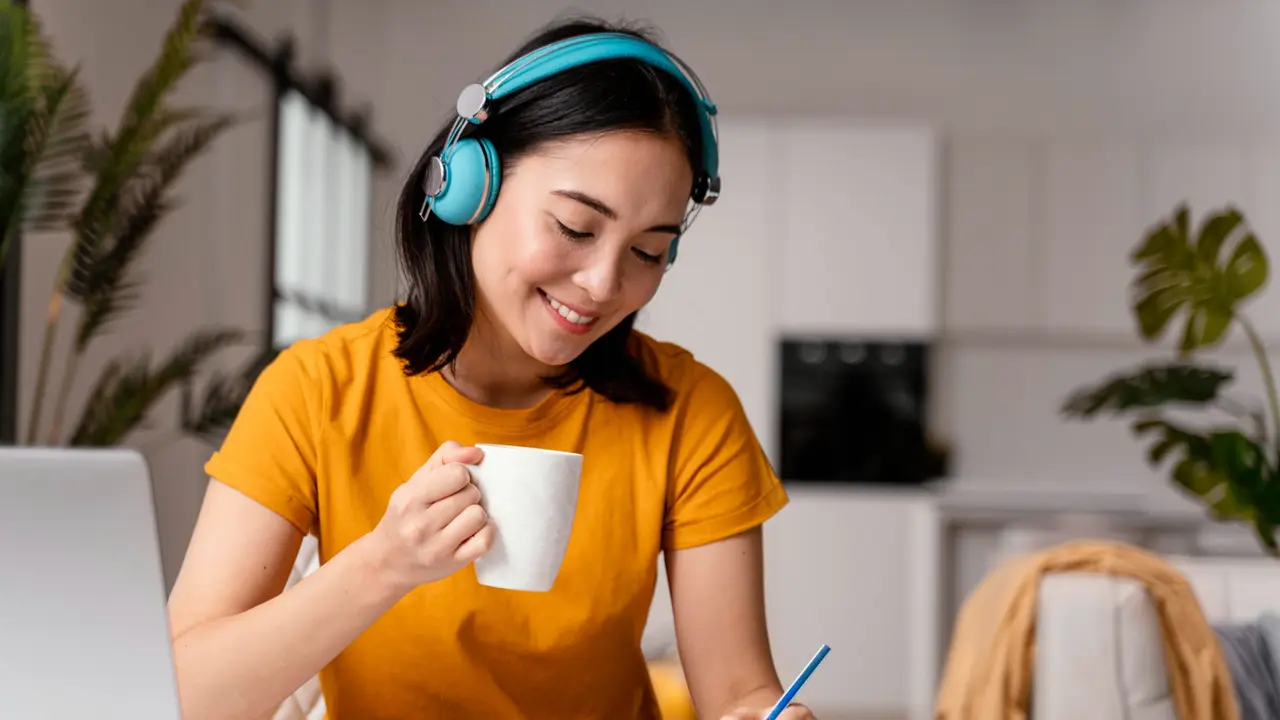 Seorang Wanita Sedang Journaling Sambil Mendengarkan Musik dan Minum Segelas Teh