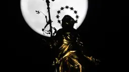 Fenomena super snow moon terlihat di belakang patung Perawan Maria 'Madonnina' di atas Katedral Duomo, Milan, Italia, Selasa (19/2). Super snow moon membuat langit berada di paras paling terang sepanjang tahun. (AP Photo/Luca Bruno)