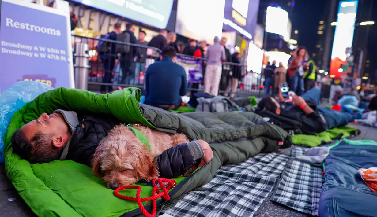 Seorang pria memeluk seekor anjing saat para aktivis mengadakan "tidur bersama" untuk meningkatkan kesadaran akan Bulan Kesadaran Tunawisma Pemuda, di Times Square, New York City, pada 16 November 2023. (KENA BETANCUR/AFP)