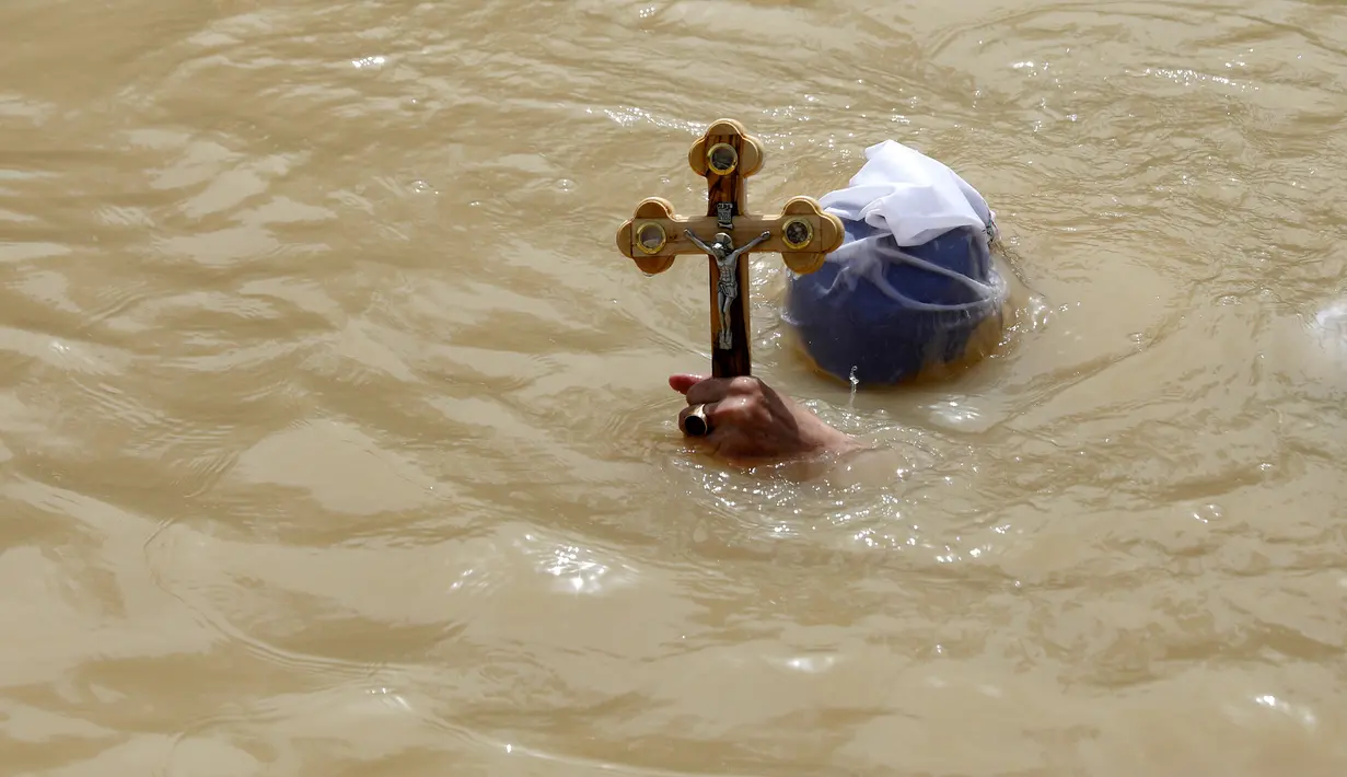 Seorang Kristen Ortodoks Moldovian membawa salib saat pembaptisan di perairan Sungai Yordan di dekat kota Jericho (4/3). Sungai ini diyakini menjadi tempat Yesus Kristus dibaptis oleh Yohanes Pembaptis. (AFP Photo/Gali Tibbon)