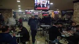 Warga Palestina berada di kafe di kota Ramallah di Tepi Barat saat sebuah siaran televisi menayangkan pidato Presiden AS, Donald Trump mengumumkan AS mengakui Yerusalem sebagai ibu kota Israel (6/12). (AFP Photo/Abbas Momani)