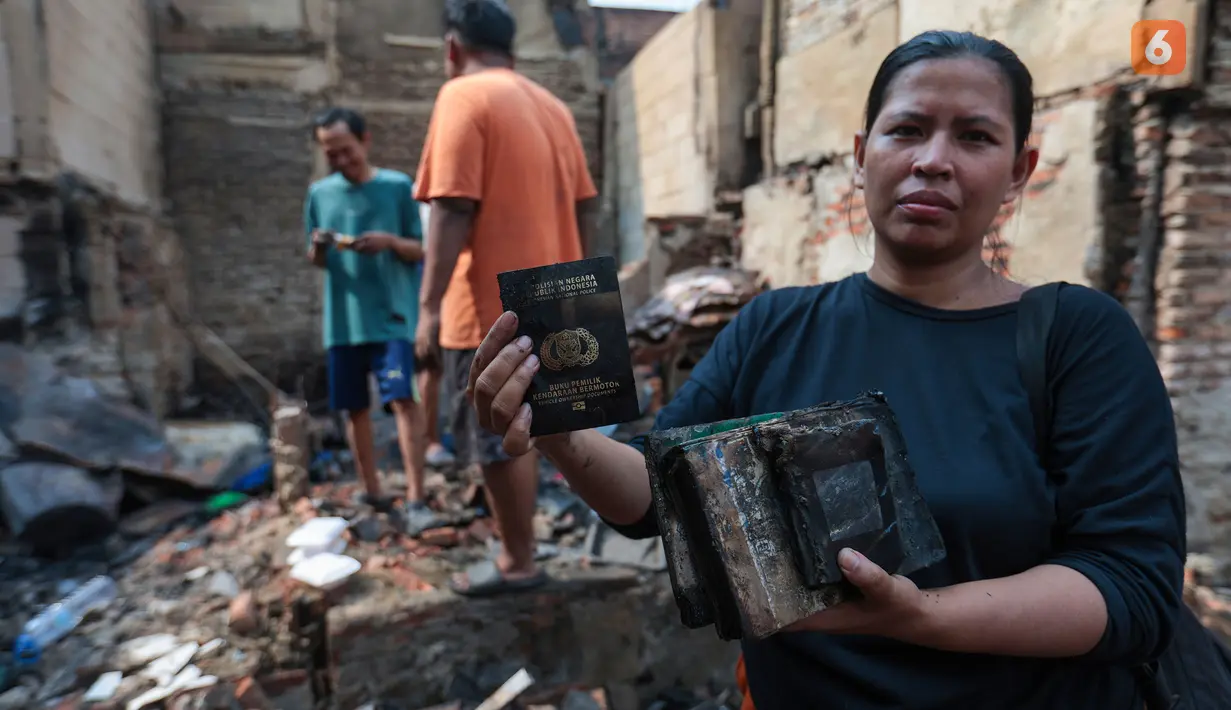 Seorang warga memperlihatkan surat-surat kendaraan bermotor yang hangus terbakar saat kebakaran melanda permukiman di Jalan Kramat Pulo Dalam, Senen, Jakarta Pusat, Jumat (9/10/2026). (KLY/Budy Santoso)
