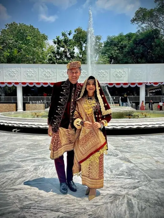 Nirina Zubir dan Ernest kompak mengenakan pakai adat Koto Gadang warna merah maroon keemasan. [Instagram/nirinazubir_]