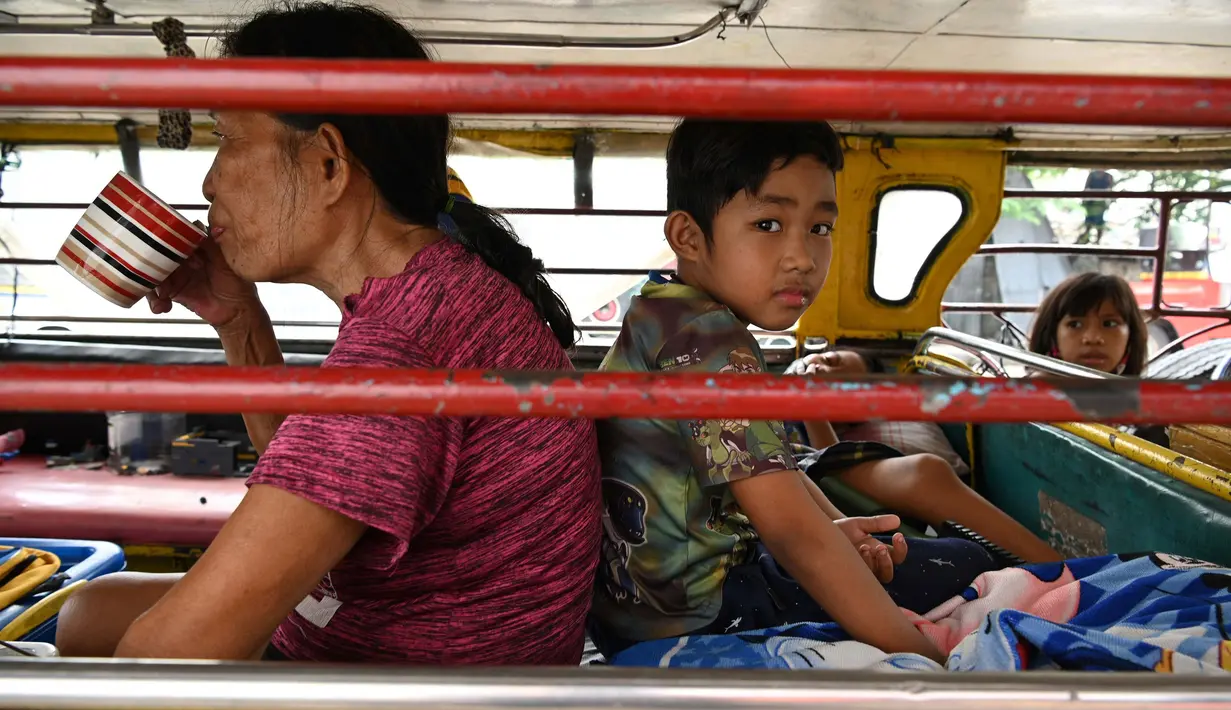 Seorang perempuan, Flores minum kopi di samping cucunya di dalam jeepney yang berfungsi sebagai rumah sementara di Manila, 12 Agustus 2020. Angkutan ikonik di Filipina itu belum dapat mengangkut penumpang sejak Maret akibat lockdown yang membuat jutaan orang kehilangan pekerjaan. (Ted ALJIBE/AFP)