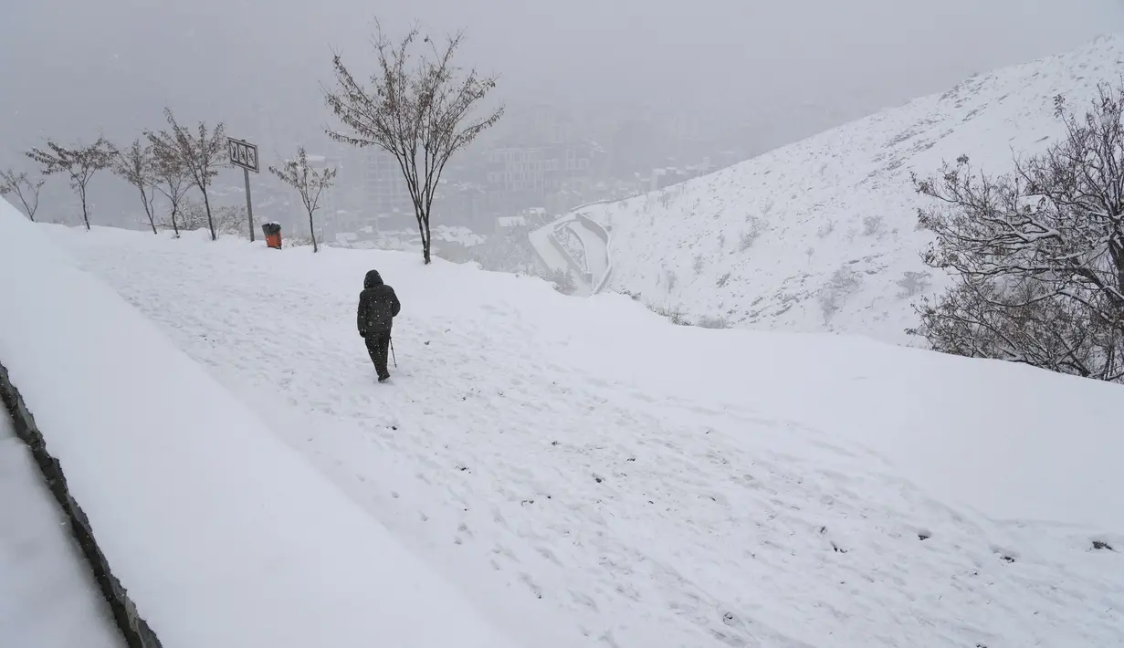Seorang pria berjalan turun di Kompleks Olahraga dan Rekreasi Tochal yang bergunung-gunung saat salju turun, di utara Teheran, Iran (24/12/2022). Salju dan hujan membawa kebahagiaan bagi banyak orang yang khawatir kekurangan air di Iran, negara yang telah mengalami kekeringan selama beberapa dekade. (AP Photo/Vahid Salemi)