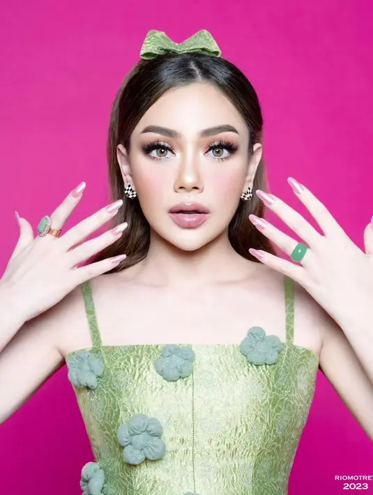 Rambutnya masih ditata sama, namun kali ini diberi pemanis pita berwarna hijau yang serasi dengan outfitnya. Riasan wajahnya bold dengan warna bibir merah muda keunguan yang glossy. [Foto: Instagram/riomotret]