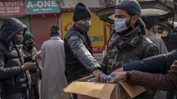 Seorang pria membagikan botol pembersih selama penguncian akhir pekan di Srinagar, Kashmir yang dikuasai India, Sabtu (15/1/2022). Pihak berwenang di bagian Kashmir India mengumumkan pembatasan penuh pergerakan yang tidak penting selama akhir pekan untuk mengekang COVID-19. (AP Photo/Dar Yasin)