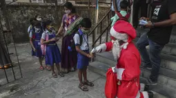 Seorang pria berkostum Sinterklas memeriksa suhu siswa setibanya mereka untuk memulai kelas di sebuah sekolah di Mumbai, India, Rabu (15/12/2021). Setelah ditutup selama hampir 20 bulan karena pandemi virus corona, sekolah di Mumbai dibuka kembali untuk kelas 1 sampai 7. (AP Photo/Rafiq Maqbool)