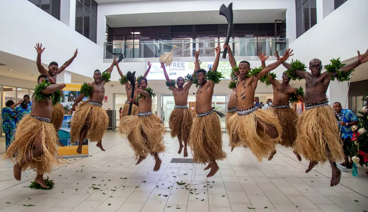 Penari tradisional dengan rok rumput menyambut wisatawan di Nadi, Fiji, Rabu (1/12/2021). Fiji membuka perbatasannya untuk pelancong internasional pertama kalinya sejak pandemi Covid-19 melanda dunia dan menghancurkan ekonominya yang bergantung pada pariwisata. (Leon LORD/AFP)