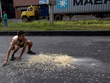 Seorang pemuda mengumpulkan biji-bijian jagung yang jatuh dari sebuah truk akibat dijarah di luar pelabuhan di Puerto Cabello, Venezuela, Selasa (30/1). Venezuela tengah menghadapi krisis ekonomi yang cukup parah. (AP Photo/Fernando Llano)