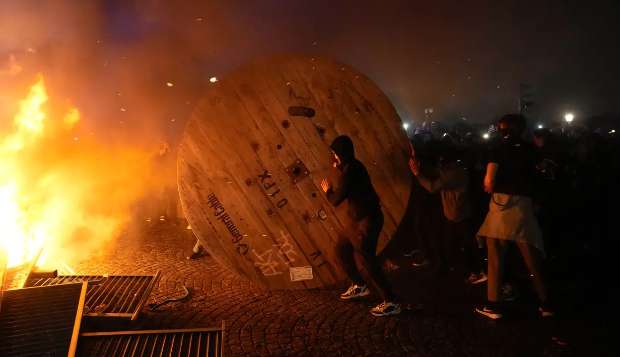 Demonstran menggulung gulungan kabel kayu ke barikade yang terbakar saat protes RUU Pensiun di Paris, Prancis, Jumat (17/3/2023). (AP Photo/Lewis Joly)