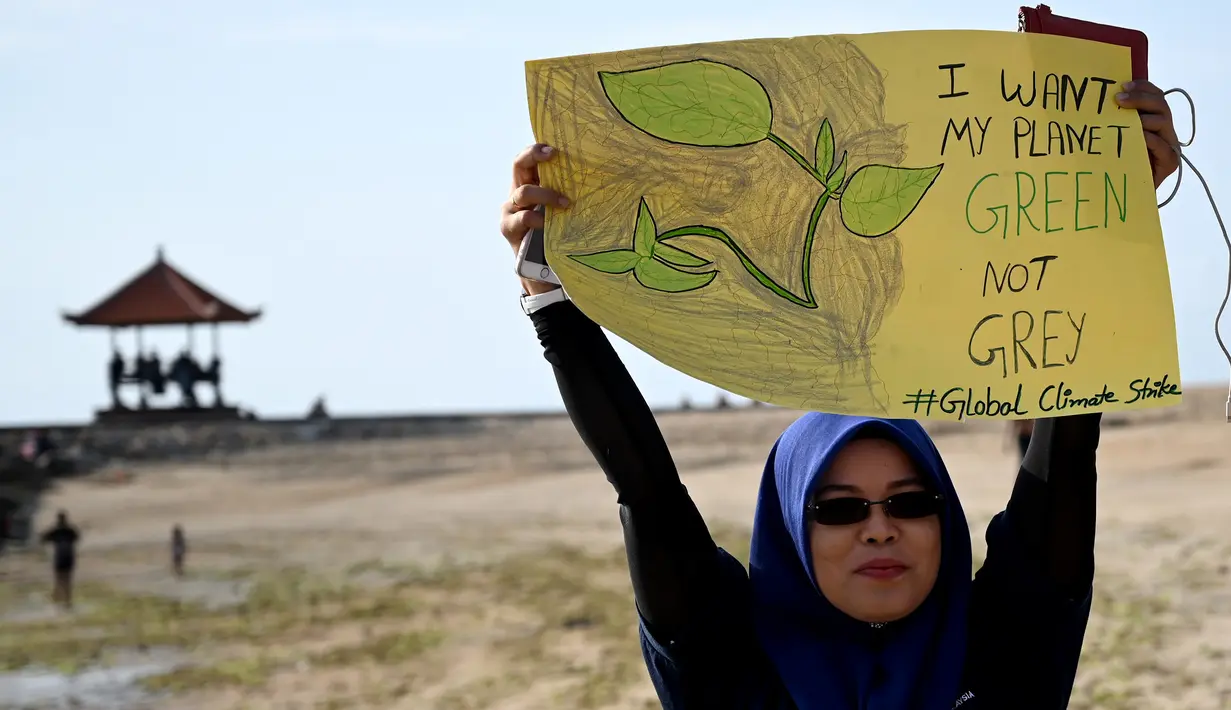Seorang wanita mengangkat plakat saat kampanye perubahan iklim global di Pantai Sanur, Bali, Jumat (20/9/2019). Massa melawan pendekatan ekonomi global yang menghasilkan emisi sangat tinggi di seluruh dunia. (SONNY TUMBELAKA/AFP)